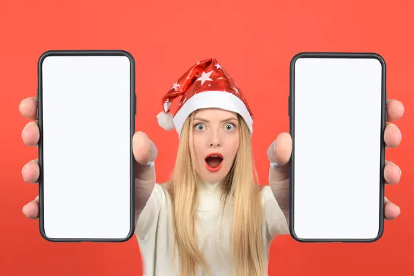 Noel Baba şapkalı, beyaz ekranlı akıllı telefonu gösteren sürpriz bir kadın.