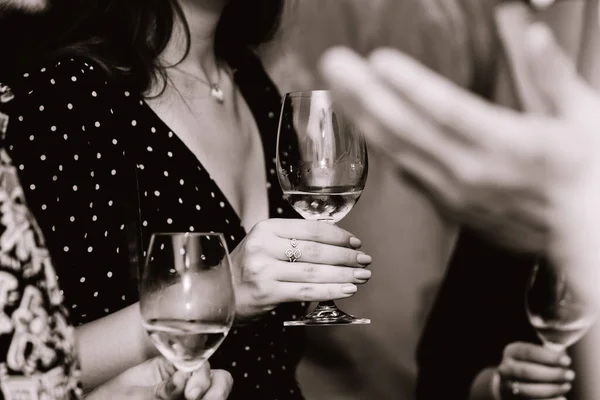 Glass of white wine held by a person at a premium wine tasting with friends and loved ones.