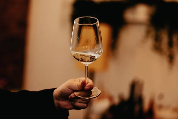 Glass of white wine held by a person at a premium wine tasting with friends and loved ones.