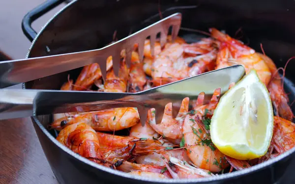 Akşam yemeği için Akdeniz yemeği. Limonlu kızarmış kral karidesleri ve siyah tavada gerbanlar..