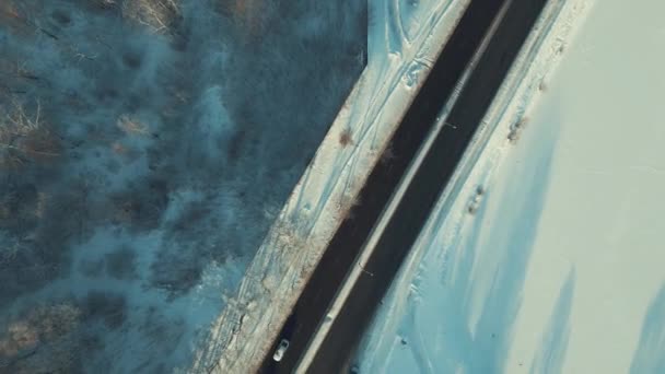 日当たりの良い冬の午後に通りを飛ぶドローン公共道路を通過する車 冬のドローン 雪と太陽 道路上の車 木の影 — ストック動画