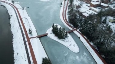Drone Winter Görüntüleri. Şehir merkezinde, ortasında ağaçlar olan bir ada olan donmuş bir göl. Sinema Drone Kış Görüntüleri. Kar, Buz, Donmuş Göl, Bulutlar. Evler ve Sokaklar.