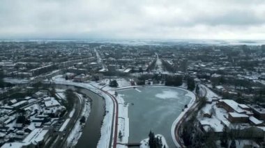 Drone Winter Görüntüleri. Şehir merkezinde donmuş bir göl. Yakınında bir nehir var. Sinema Drone Kış Görüntüleri. Kar, Buz, Donmuş Göl, Bulutlar. Evler ve Sokaklar.