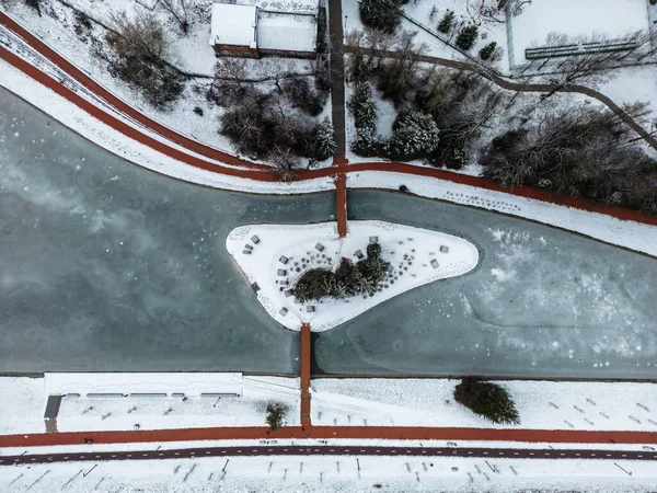 Drone Winter Görüntüleri. Şehir merkezinde, ortasında ağaçlar olan bir ada olan donmuş bir göl. Sinema Drone Kış Görüntüleri. Kar, Buz, Donmuş Göl, Bulutlar. Evler ve Sokaklar.