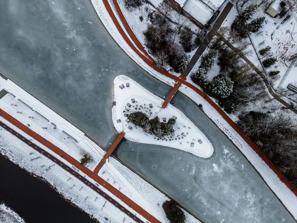Drone Winter Footage. Frozen Lake In The City Center With An Island In The Middle With Trees. Cinematic Drone Winter Footage. Snow, Ice, Frozen Lake, Clouds. Houses And Streets.