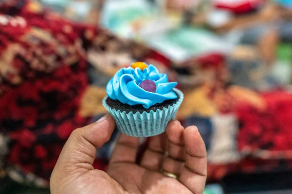 Homemade chocolate cupcake with blue topping held by hand.