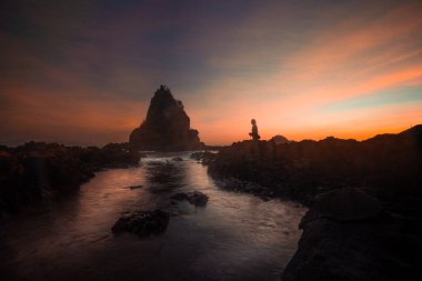 A breathtaking view of Diguisit Rock Formation at sunset, where rugged, weathered rocks in the foreground glow with warm orange hues. A small, tranquil pool reflects the serene beauty of the scene, while dramatic rock formations, including a pointed  clipart