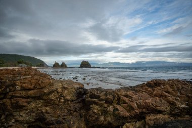 Stunning Diguisit Beach in Baler, Philippines. It features a rugged coastline lined with rocky formations and a serene seascape. The foreground showcases weathered rocks leading to the iconic Diguisit rock formations, dramatically positioned against 