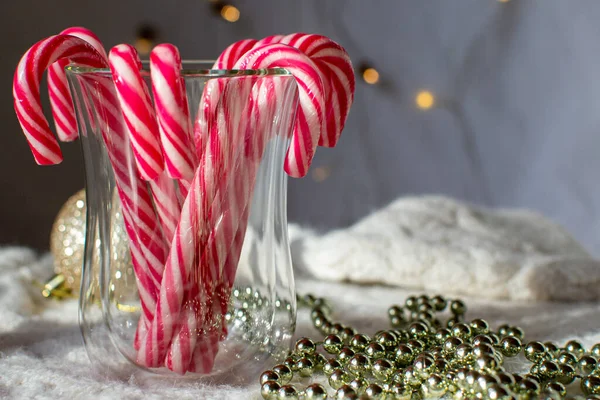 Kırmızı ve beyaz karamel çubuklar bir bardakta arka planda ışıklar ve Noel ağacı süslemeleri