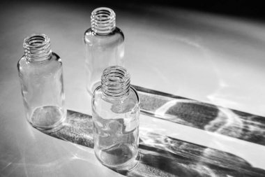 Empty glass bottles from under cosmetics cast a shadow on a white table