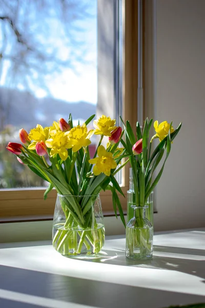 Glass vases with spring flowers on a white table near the window