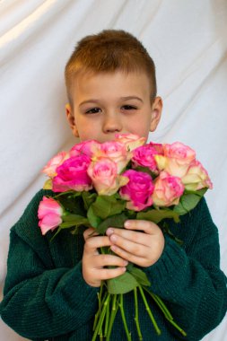 A little boy in a green sweater gives a bouquet of pink roses