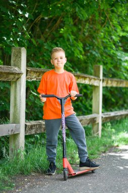Sarı saçlı ve motosikletli turuncu tişörtlü genç bir çocuk.