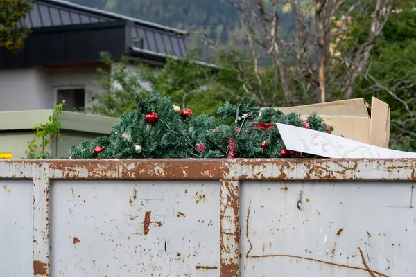 Çöpe atılmış plastik köknar ağaçları çöp konteynırında kırmızı Noel toplarıyla süslenmiş..