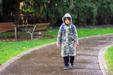 Okul çantalı yağmurluk giyen bir çocuk yağmurda okula gider..