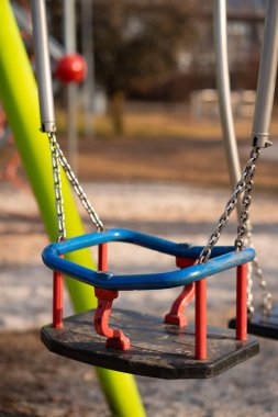 Çocuklar şehir parkında metal ve plastikten yapılmış salıncaklar sallıyorlar..