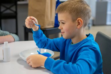Masada mavi süveterli bir çocuk mavi salya yapıyor..