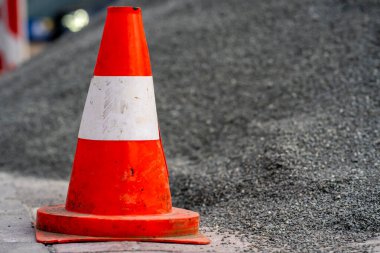Bir inşaat alanındaki çakıl dağının yanında duran turuncu bir trafik konisi görülüyor.