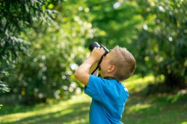 Mavi tişörtlü yakışıklı çocuk parkta kamerayla fotoğraf çekiyor..