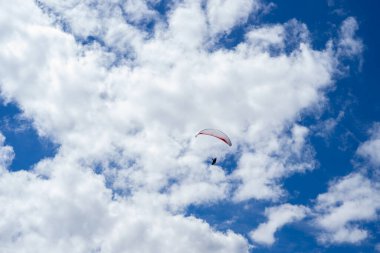 Tek başına bir paraglider parçalı bulutlu bir gökyüzünde canlı mavi tonlarda süzülür. Özgürlüğün, ekstrem sporların ve doğadaki maceranın mükemmel bir görüntüsü..