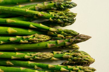 Güneş ışığında beyaz bir masada sıralanmış taze yeşil kuşkonmaz manzarası.