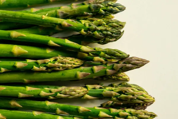 Güneş ışığında beyaz bir masada sıralanmış taze yeşil kuşkonmaz manzarası.