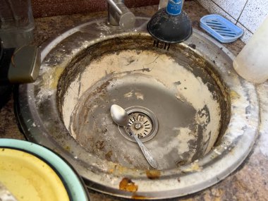 Büyük metal mutfak lavabosu kireç pulu ve kirli tabaklarla kaplı bir katman.