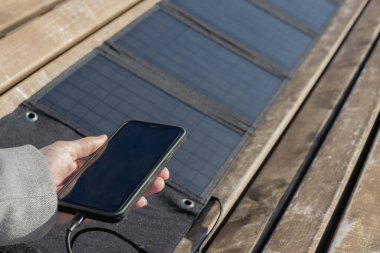 Güneş paneline bağlı telefonu tutan bir kadın. Güneş paneli