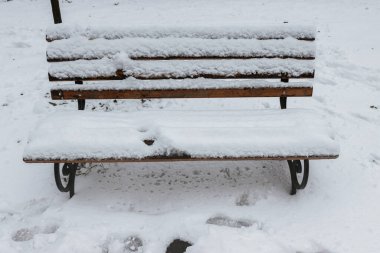 Park bankları ve ağaçlar yoğun karla kaplı. Karla kaplı eski bir bank.