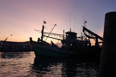 İskelenin üzerinde sakin bir günbatımı ve yumuşak akşam ışığı ile rıhtıma yanaşmış balıkçı tekneleri.