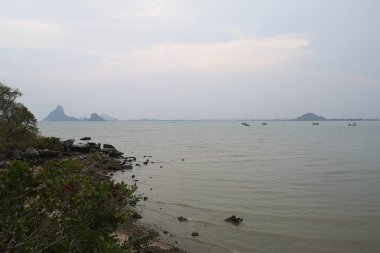 Okyanusun üzerindeki mavi gökyüzünde beyaz bulut kıyı şeridi ve dağları manzaralı.