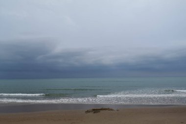 Fırtınalı bir sahil sahnesi. Çarpan dalgalar ve denizin üzerinde kara bulutlar.