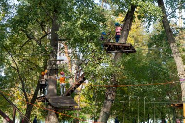 Ukraine, Kyiv-October 2022: Children play in the rope park among the forest. Child in the forest adventure park. Children in protective helmets walk along the cable car high among the trees. High