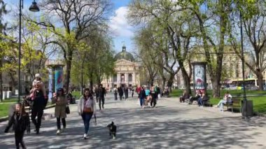 Lviv, Ukrayna - 18 Nisan 2023: Güneşli bir günde Opera Tiyatrosu yakınlarındaki parkta yürüyen insanlar. Ukrayna 'nın Lviv şehrindeki güzel şehir hayatı. - Evet. Yüksek kalite 4k görüntü