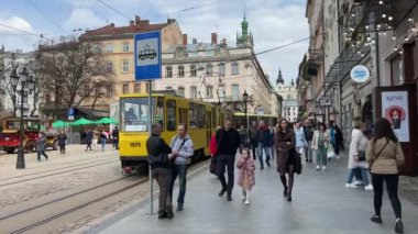 Lviv, Ukrayna - 18 Nisan 2023: Lviv sokaklarında insanlar. Vatandaşlar ve turistler Lviv 'deki Pazar Meydanı' nda yürüyüp dinleniyorlar. Şehir merkezinde eski bir tramvay. Yüksek kalite 4k görüntü