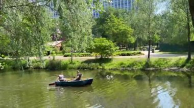 Ukrayna, Kyiv - Haziran 2023: İnsanlar şehir parkındaki bir nehirde kiralık bir tekne kullanıyorlar. Esinti söğütleri sallıyor. Yüksek kalite 4k görüntü
