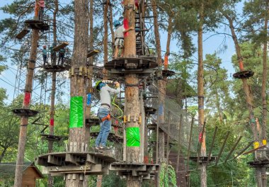 Çocuklar ormanın arasındaki ip parkında oynuyorlar. Orman macera parkındaki çocuk. Koruyucu kasklı çocuklar ağaçların arasında teleferik boyunca yürüyorlar. Yüksek kalite fotoğraf