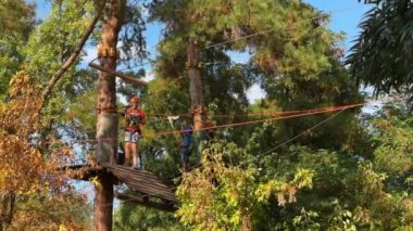 Ukrayna, Kyiv - 30 Eylül 2023: Çocuklar ormanın arasındaki halat parkında oynuyorlar. Orman macera parkındaki çocuk. Koruyucu miğferli çocuklar ağaçların arasında teleferik boyunca yürüyorlar.