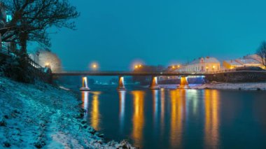 Uzhhorod 'daki kar gecesinde aydınlatılmış yaya köprüsü, güzel bir gece şehri ve kış nehri manzarası ve insanlar köprü boyunca yürüyor. Yüksek kalite 4k görüntü