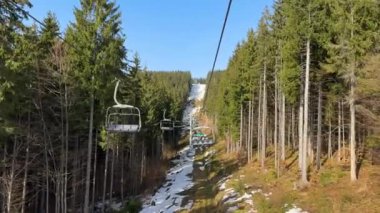 Bukovel, Ukrayna - 1 Mart 2024: Cableway, teleferikli insanlar yeşil çam ormanı arasındaki kayak yamacı boyunca ilerliyorlar. Kışın, güneşli kayak merkezinin çeşitli yönlerde asansörleri vardır. Yüksek kalite 4k