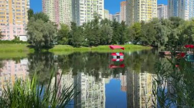 Şehir parkındaki bir gölün ışık dalgaları üzerinde kırmızı bir katamaran yüksek binaların arka planına karşı. Yüksek kalite 4k görüntü