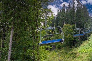 Boş bir asansör yazın güneşli bir dağ beldesine iniyor. Çam ormanının arka planına karşı. Kablo yokuş aşağı, arka planda gökyüzü olan sandalye kaldırma. Yüksek kalite fotoğraf