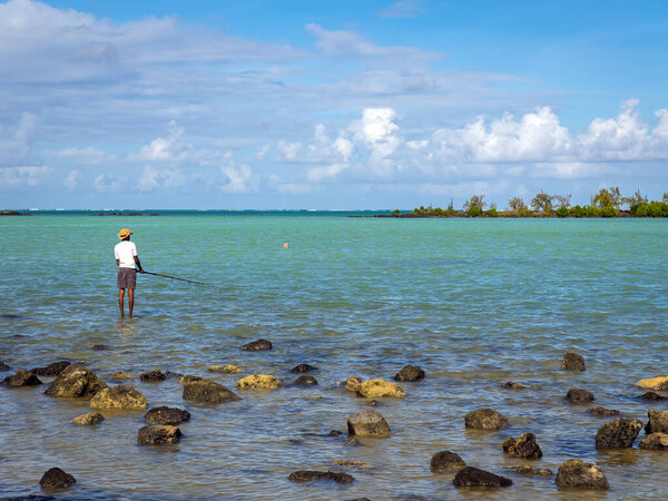 Shore fishing in tropical paradise. Local angler standing in clear waters. Person casting line in shallow lagoon. Coastal livelihood. Traditional Fishing Methods. High quality photo