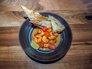 Kızarmış ekmekle sarımsaklı karides, kara tabakta kiraz domatesleri ve limonlu karides. Gurme karides aperatifi: Sarımsaklı karides ve kızarmış taze domates. Yüksek kalite fotoğraf