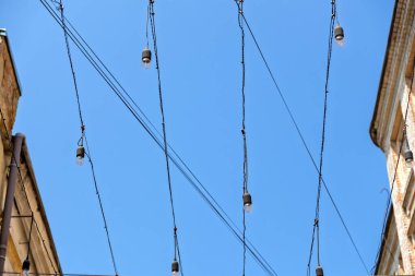 Dekoratif Sicim Işıkları Garland 'ı eski binaların arasında asılı duran berrak bir çatı ile süslüyor. Şehir sokak dekorasyonu: Bir sokak lambası gündüz vakti gökyüzüne karşı bir sokak boyunca gerildi