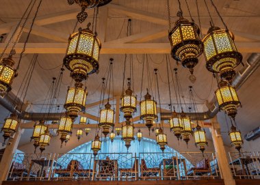 Egzotik Atmosfer: süslü Fas fenerlerinin çarpıcı kurulumu rahat bir restoranın içini aydınlatır. Otantik Ortadoğu Ambiansı: Süslü metal fenerler asma katlı oturma alanının üzerinde asılı