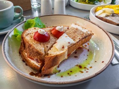 Lezzetli ve rahatlatıcı bir brunch: Eritilmiş peynirli ve domatesli kızarmış ekşi sandviç, bir restoranda süslenmiş ve güzelce kaplanmış. Yüksek kalite fotoğraf