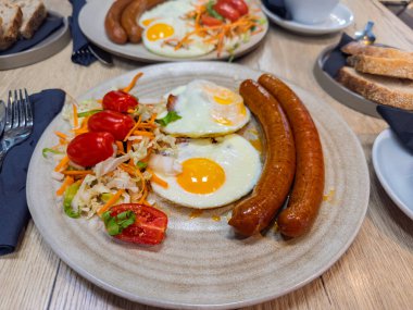 İki kişilik kahvaltı bir tabak sahanda yumurta, baharatlı sosis ve sağlıklı bir salata üzerine odaklanarak bir restoranda servis edilir.