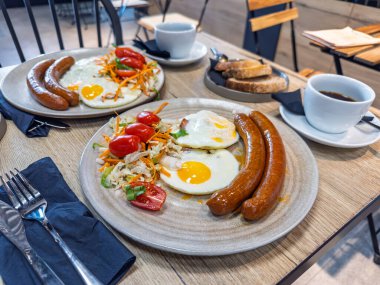 Modern bir kafede iki kişilik nefis bir kahvaltı, kızarmış yumurta, sosis, taze salata ve kahve. İki kişilik hafta sonu brunch 'ı.