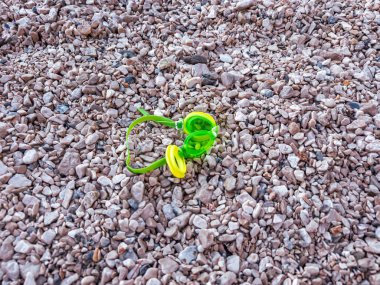 Yaz tatili konsepti: kayalık bir kıyının dokulu taşlarında uzanan renkli yüzme gözlükleri. Deniz kenarında eğlenceli bir günün sonu. Sahildeki çakıl taşlarının doğal arka planında canlı yüzme ekipmanları.
